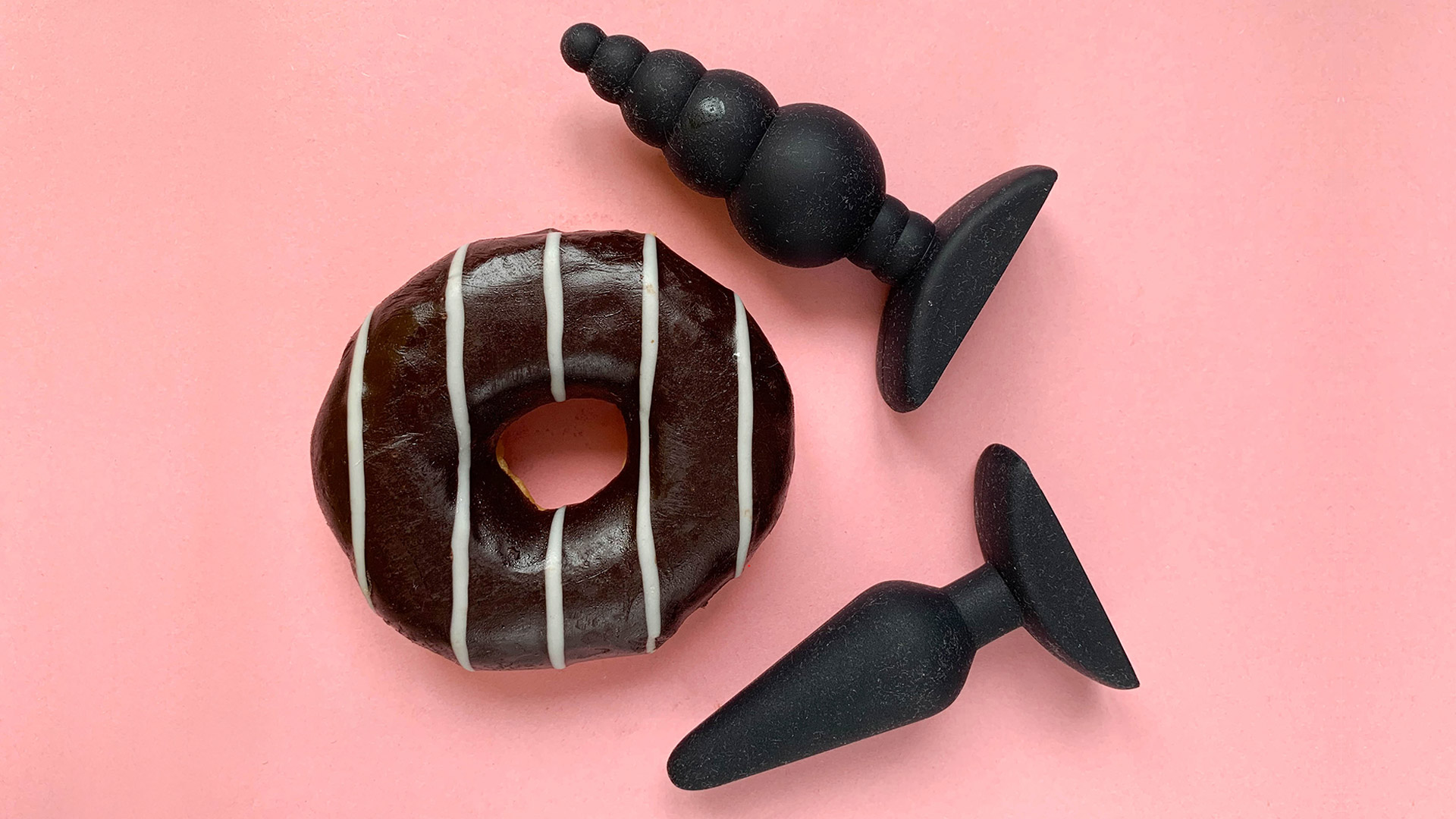 Two butt plugs with a with a black and white donut on a pink background. 