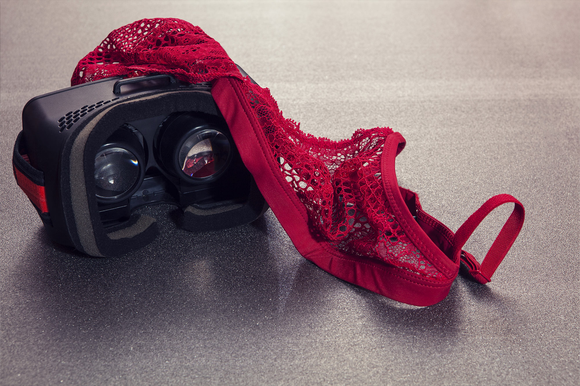 Black VR headset on the ground with red lace lingerie thrown on top of it.